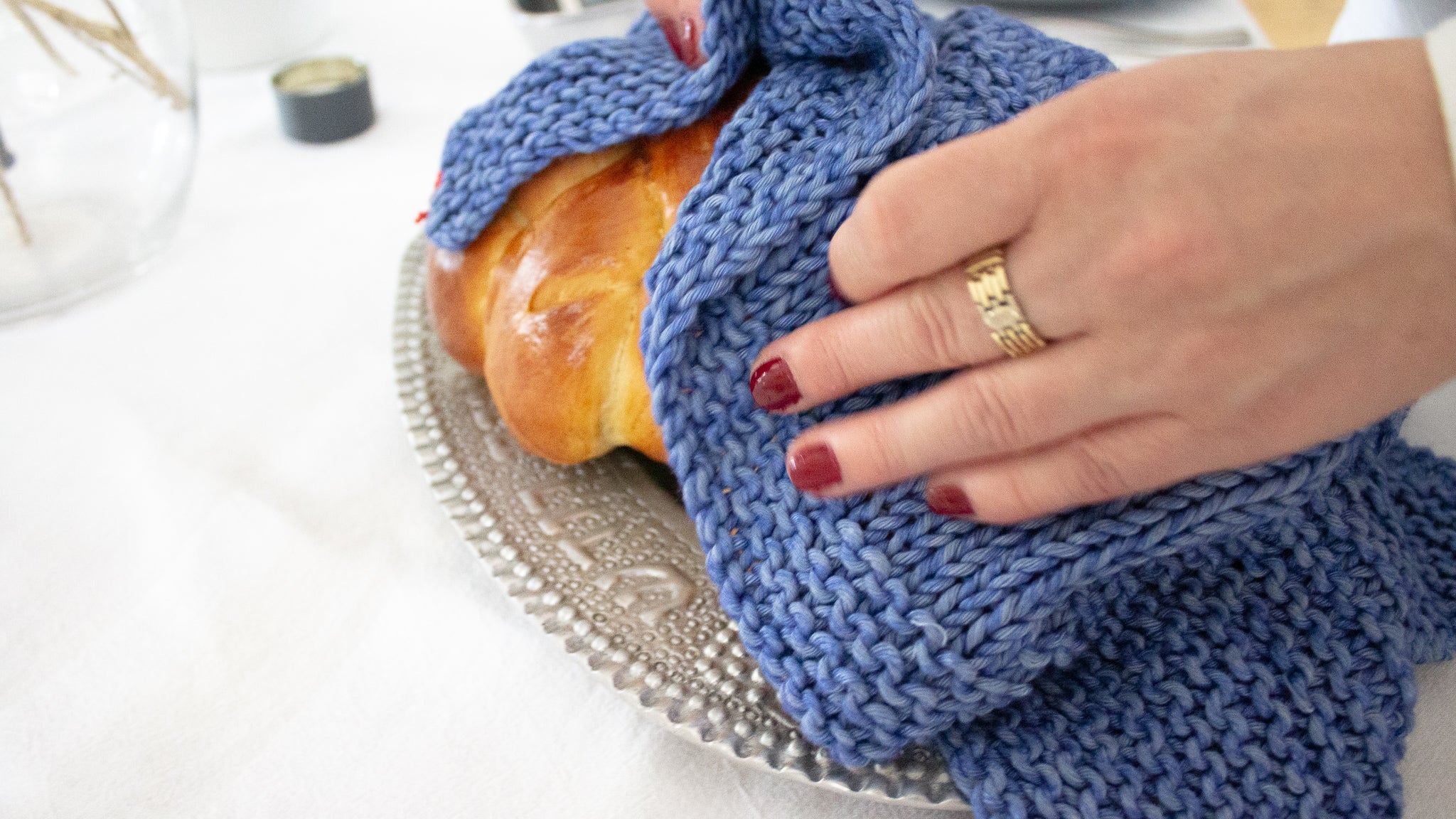 Woman with red pained nails covering challah on a silver platter with a blue Penelope D Magen David Challah Cover.