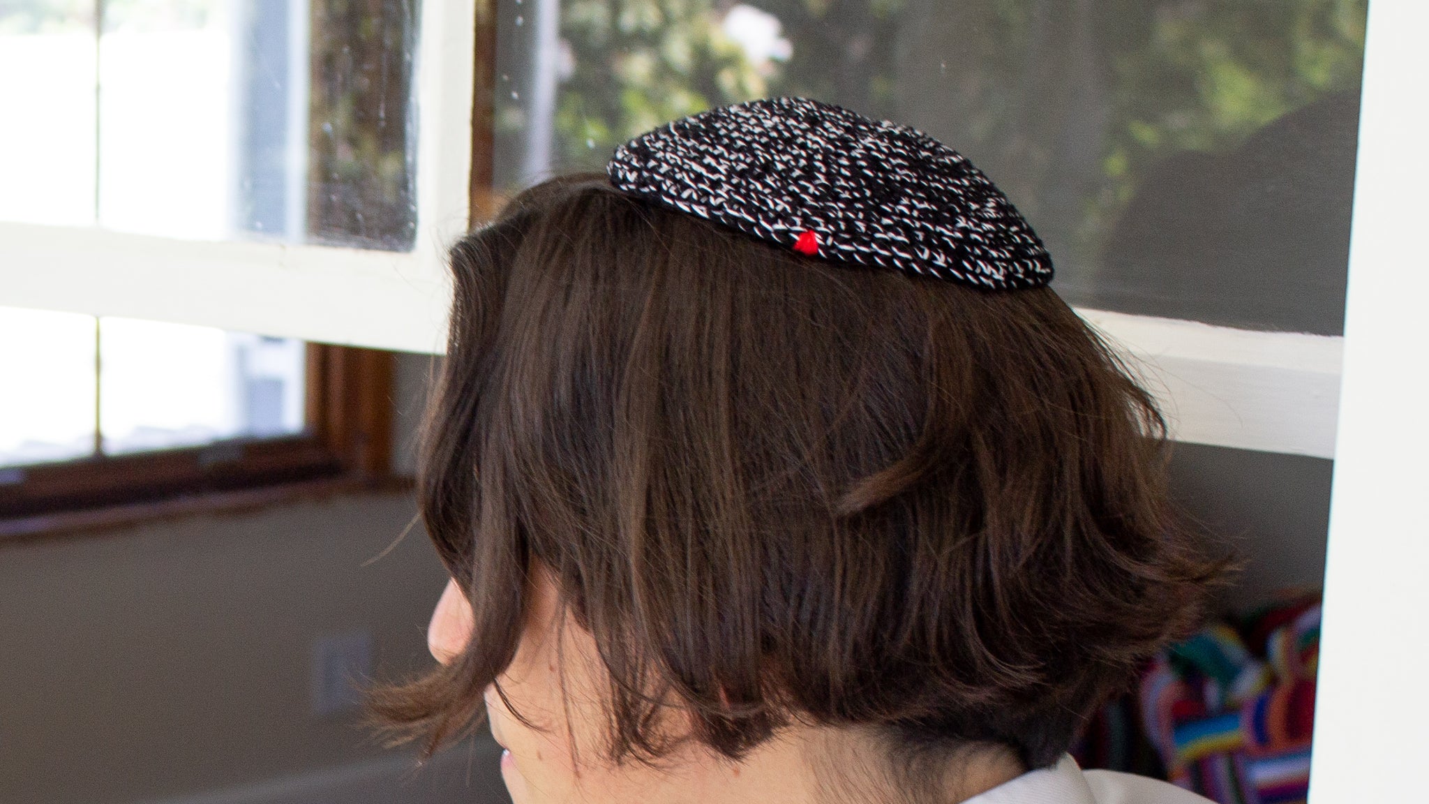 Male sitting outside, in-front of a window with his Penelope D Judaica, black and white, Melange Kippah on his head.