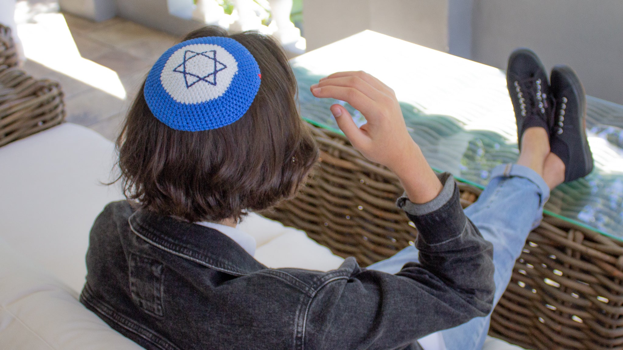 Male sitting on an outdoor couch wearing his Penelope D Judaica, Jewish Symbol Kippah with a standard Magen David star in blue & white colour combinations..