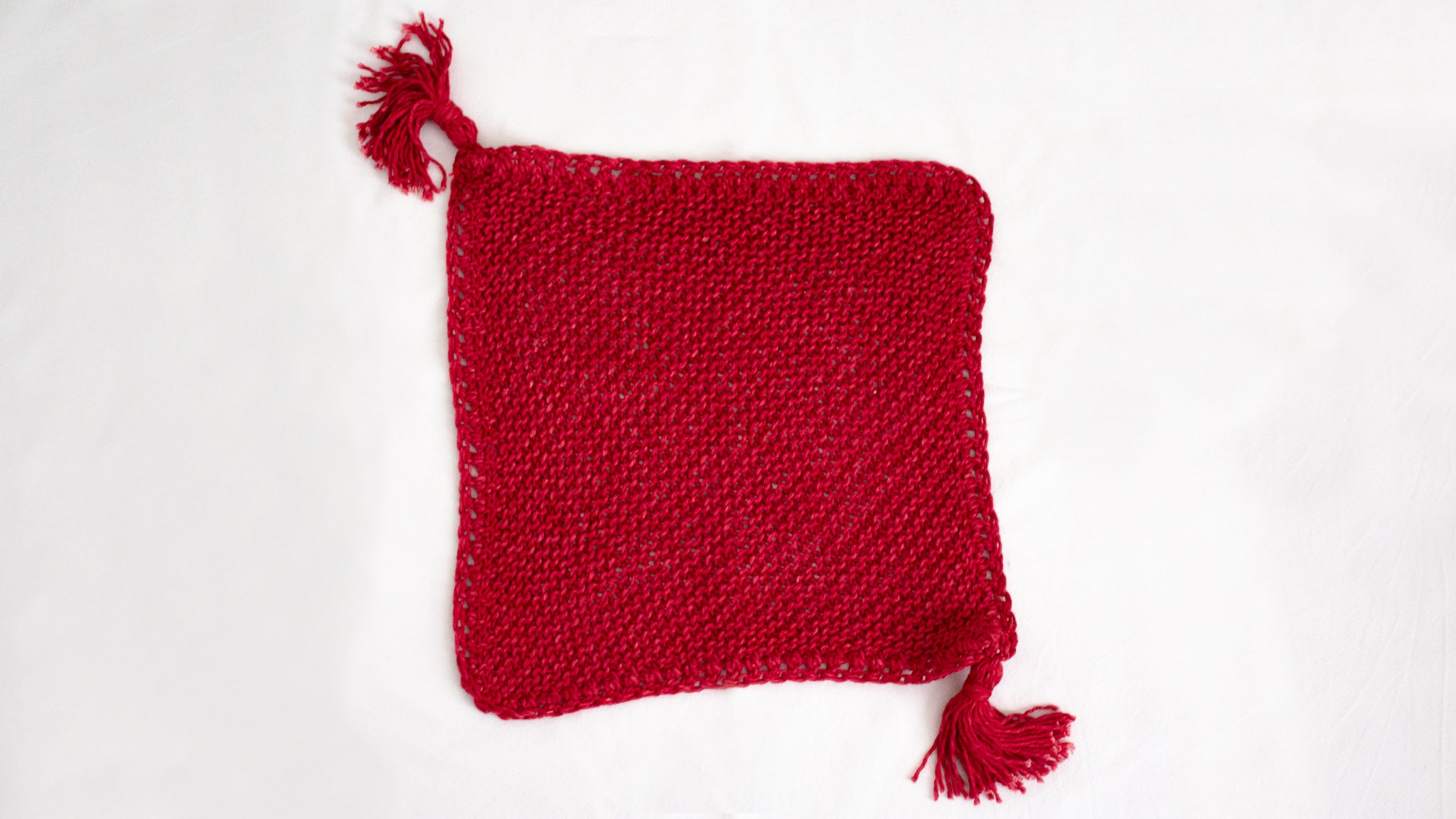 Flat lay of a Penelope D Judaica, Plain Tassel Challah Cover in raspberry with tassels.