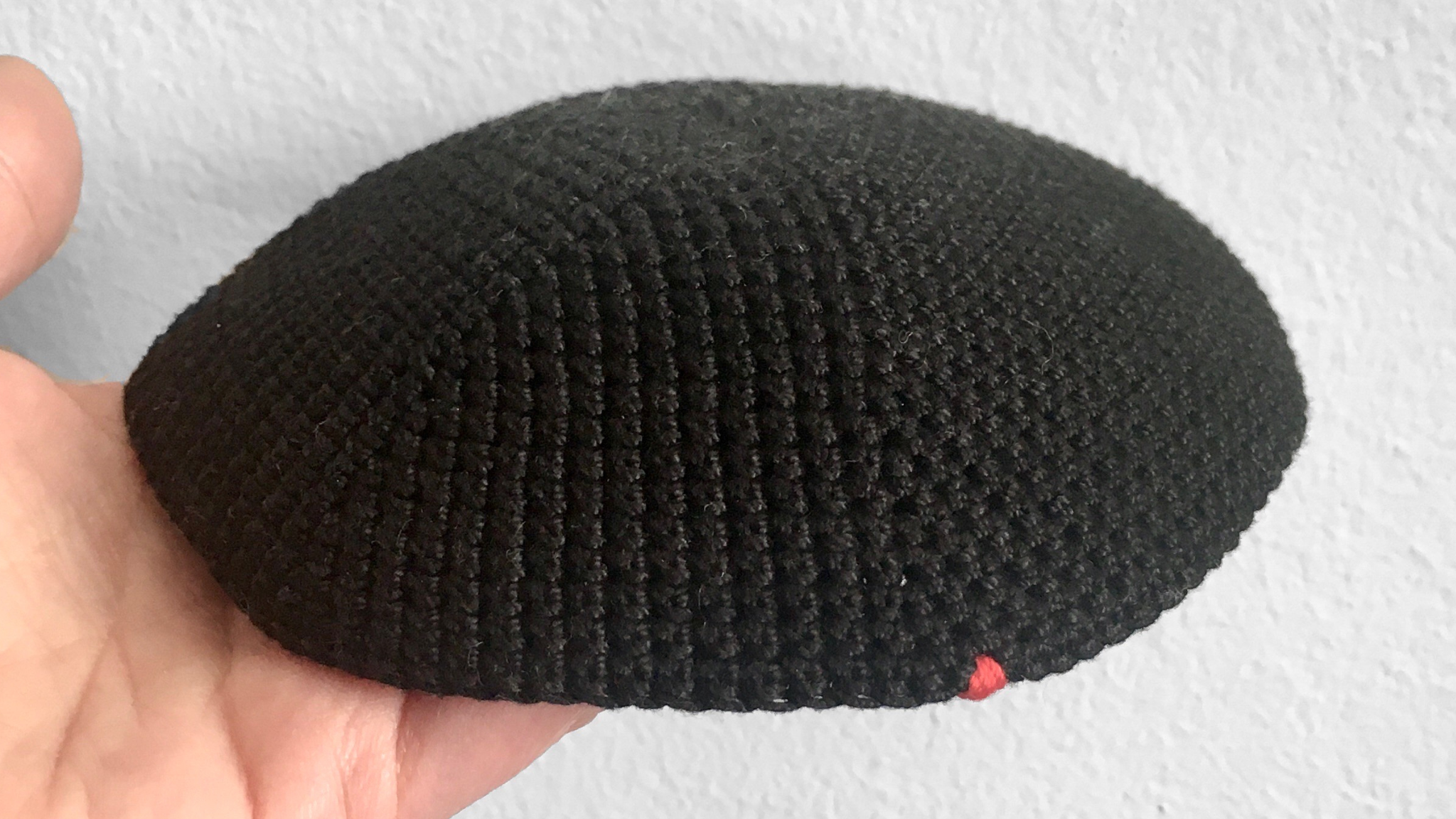 Close up of the Penelope D Thin Kippah in black, showing the Penelope D 7-thread crimson red knot mark.